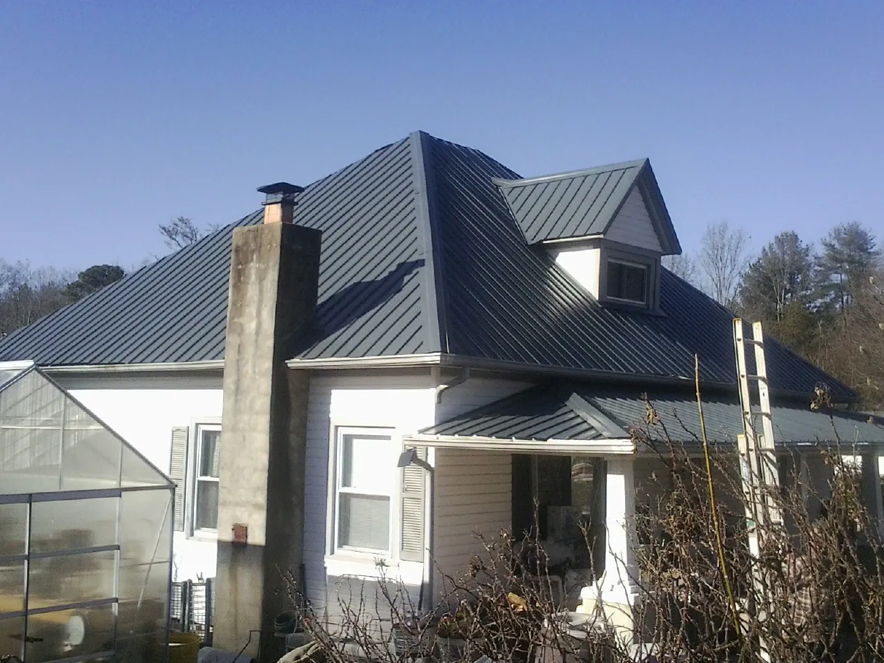 Dark blue standing seam metal roof on a white farmhouse with dormer — Slate & Tile Roof Repair by Roofing Brothers in Manhattan