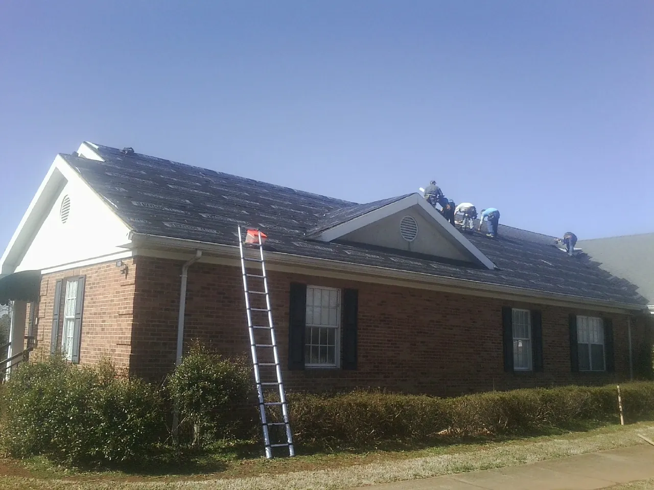 Crew tearing shingles off a brick ranch roof with a ladder set — Metal Roof Repair work by our crew in Manhattan