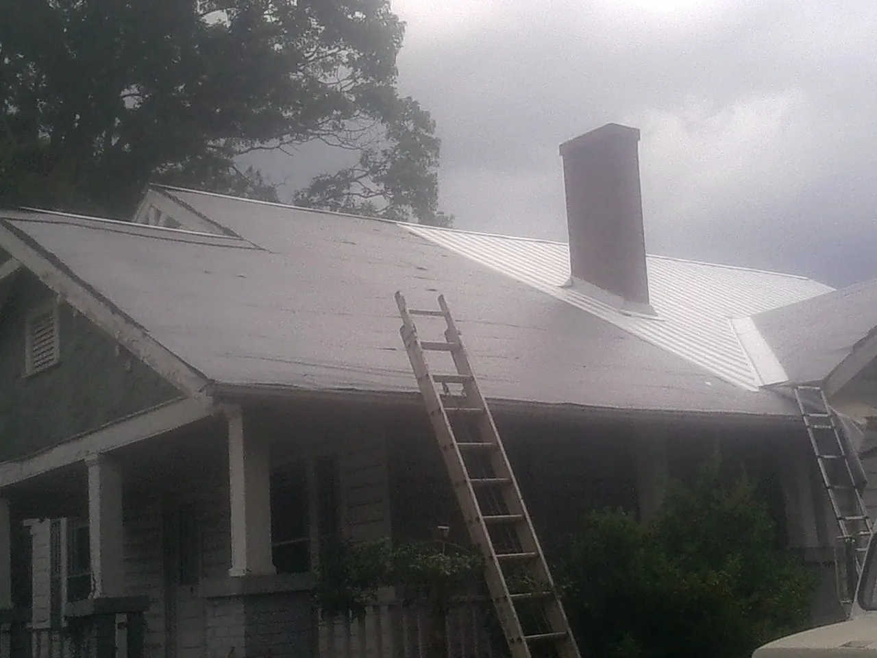 Ladders against a metal roof on an older home with a brick chimney in Manhattan